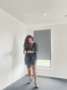 a woman in a black sequined dress and heels stands in front of a window