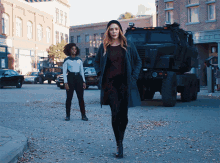 two women are walking down a street in front of a military vehicle that says ' us army ' on the side