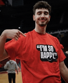 a man is wearing a red t-shirt that says `` i 'm so happy '' and pointing at his arm .