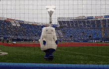 a mascot stands on a baseball field in front of a stadium full of blue seats and a sign that says eva