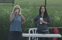 two women are standing next to each other on a bench in a park .