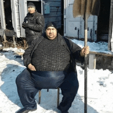 a man sitting on a chair in the snow holding a shovel