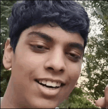 a close up of a young man 's face with a smile on his face and trees in the background .