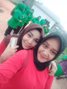 a woman in a red shirt is standing next to another woman in a black head scarf