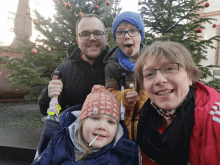 a family standing in front of a christmas tree with one child sticking out his tongue