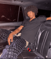 a man in a black shirt and black louis vuitton pants sits in the back seat of a car