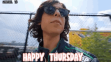 a man wearing sunglasses and a jacket is standing in front of a fence and says happy thursday .