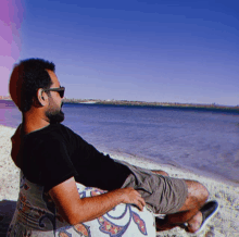 a man wearing sunglasses sits on a beach looking out over the water