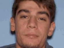 a close up of a young man 's face with a beard and a blue background .