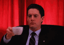 a man in a suit and tie is holding a cup of coffee in his hand .