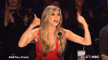 a woman in a red dress is giving a thumbs up while sitting in front of a microphone and a nbc cup