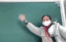 a woman wearing a mask is standing in front of a blackboard with her arms in the air .