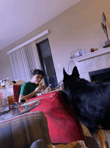 a man sits on a couch eating a sandwich while a dog looks on