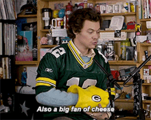 a man wearing a green bay packers jersey is holding a yellow green bay packers glove and saying also a big fan of cheese