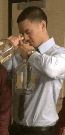 a man in a blue shirt and tie is drinking from a large bottle