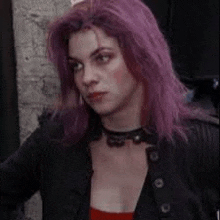 a woman with purple hair and a choker is wearing a black jacket .