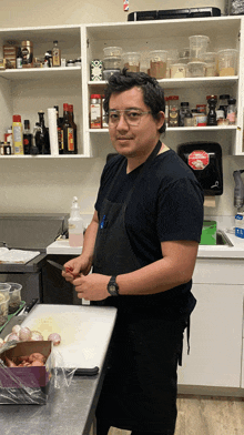 a man in a black shirt and apron is standing in a kitchen cutting onions