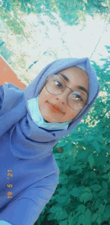 a woman wearing a hijab and glasses is taking a selfie with a mask on her face .