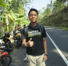 a young man wearing a national geographic t-shirt giving a thumbs up