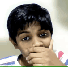 a young boy covering his mouth with his hand while wearing a striped shirt with the number 51 on it