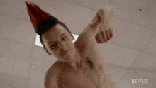 a shirtless man with a party hat on his head is holding a bottle of blood .