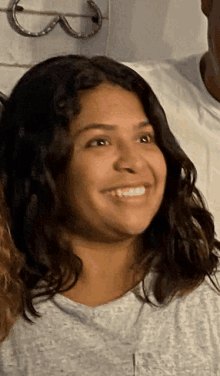 a woman in a grey shirt smiles in front of a horseshoe hanging on a wall