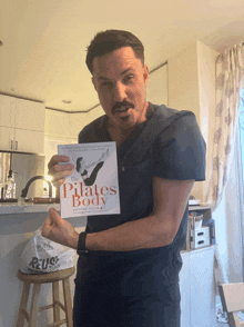 a man in scrubs holds up a book titled the pilates body