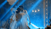 a bride and groom are dancing in a room with a blue light shining on them