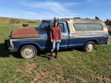 a boy in a plaid shirt stands in front of a blue pickup truck