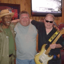 three men are posing for a picture while one of them is holding an electric guitar .