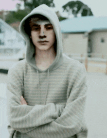 a young man wearing a striped hoodie has his arms crossed in front of a building