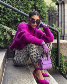 a woman wearing a purple sweater and purple gloves is sitting on steps