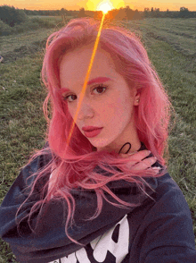 a girl with pink hair is standing in a field with the sun shining on her face