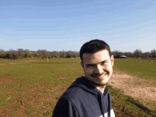 a young man with a mustache is standing in a grassy field and smiling .