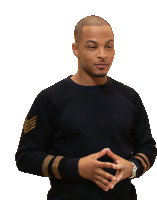 a man in a black sweater with gold stripes on the sleeves is standing with his hands folded