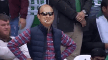 a man wearing sunglasses is smoking a cigarette while sitting in a crowd of people .