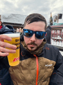 a man in a columbia jacket holds a cup of beer in his hand