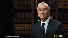 a man in a suit and tie is standing in front of a bookshelf with a nbc logo on it