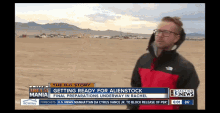 a man in a red and black jacket stands in front of a screen that says " getting ready for alienstock "