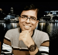 a man wearing glasses and a watch is smiling with his hand on his chin