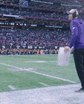 a man in a purple jacket stands on a football field with a sign that says visit mercedes benz of atlanta northeast