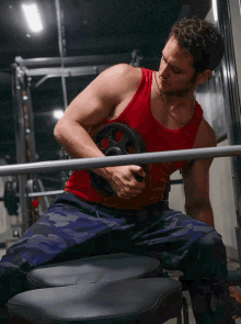 a man in a red tank top holds a barbell