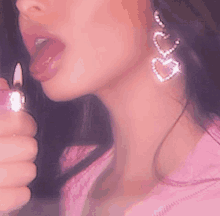 a close up of a woman lighting a lighter with her tongue out and wearing heart shaped earrings .