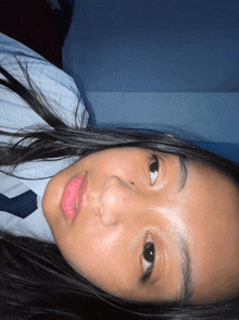 a young girl in a school uniform and tie is laying on her stomach on a bed .