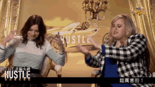 two women are standing in front of a hustle poster