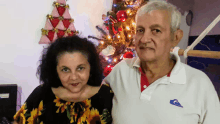 a man wearing a white quiksilver shirt poses with a woman in front of a christmas tree