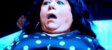 a woman with a surprised look on her face is wearing a blue and white polka dot shirt