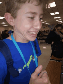 a boy wearing a blue shirt with a dinosaur on it is smiling