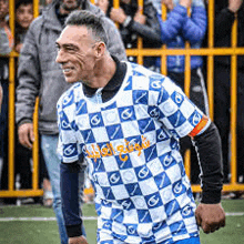 a man in a blue and white checkered soccer jersey is standing on a field .