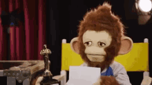 a stuffed monkey in a director 's chair holding an oscar trophy